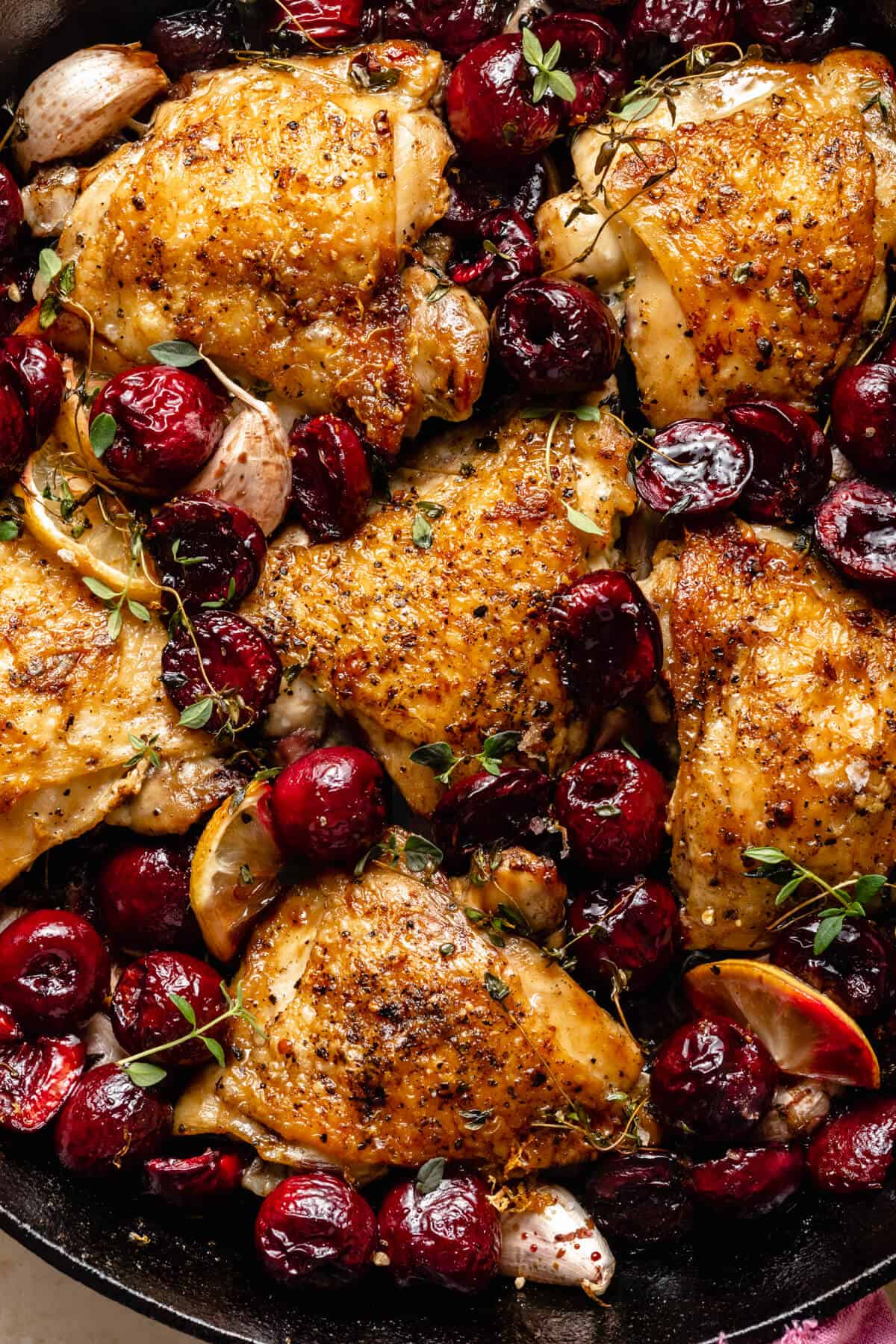 close up of crispy chicken skin and cherries surrounded with lemon slices thyme and garlic.