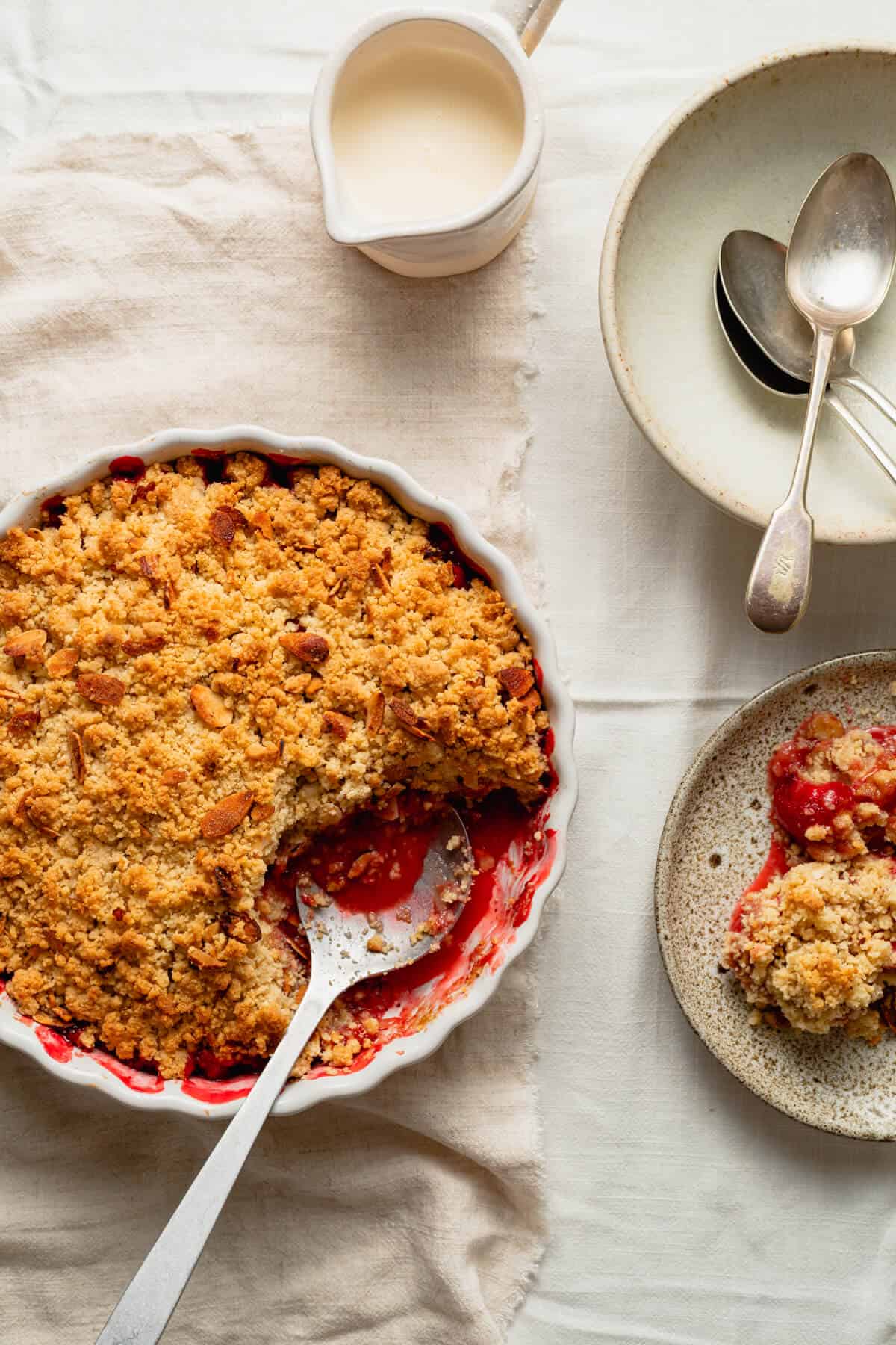 strawberry crumble baked in a flan dish and being served onto a plate with a spoon