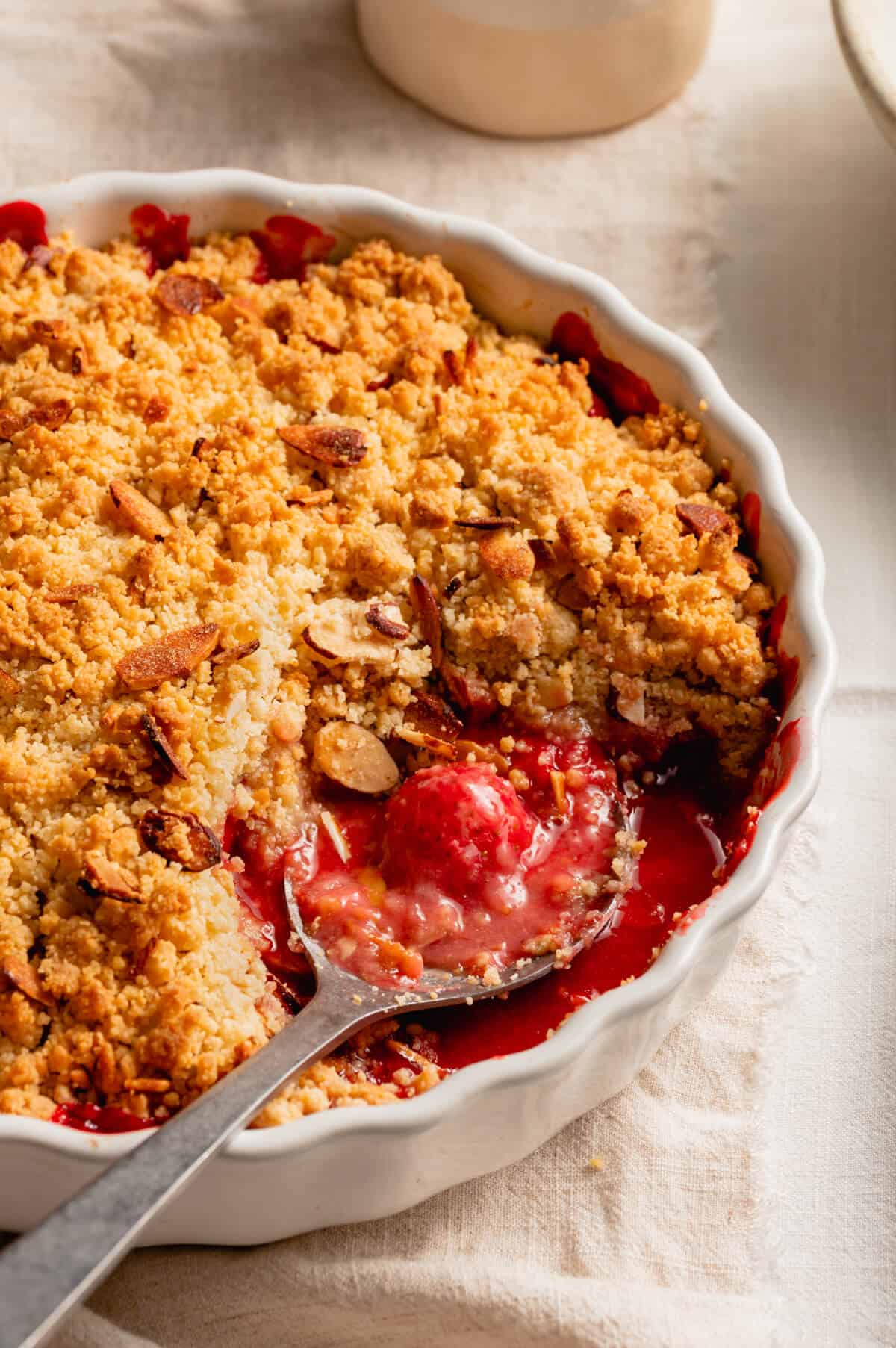 A spoon taking a serving of strawberry crumble out of the dish with it's sauce.