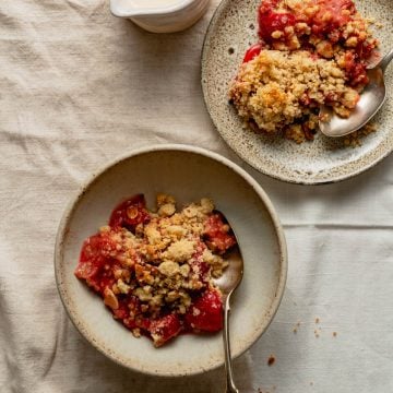 Strawberry crumble served up in a bowl and a plate with cream in a jug