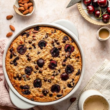 Cherry Chocolate Chip baked oatmeal in a baking dish with a mug of coffee and paper nearby.