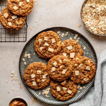 White chocolate chip oatmeal cookies on a plate with oats and biscoff in dishes to the side