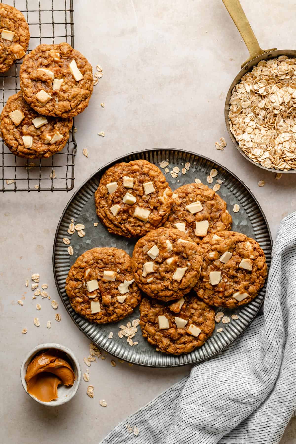 Biscoff and white chocolate chip oatmeal cookies on a plate and cooling rack, with oats and biscoff in dishes nearby