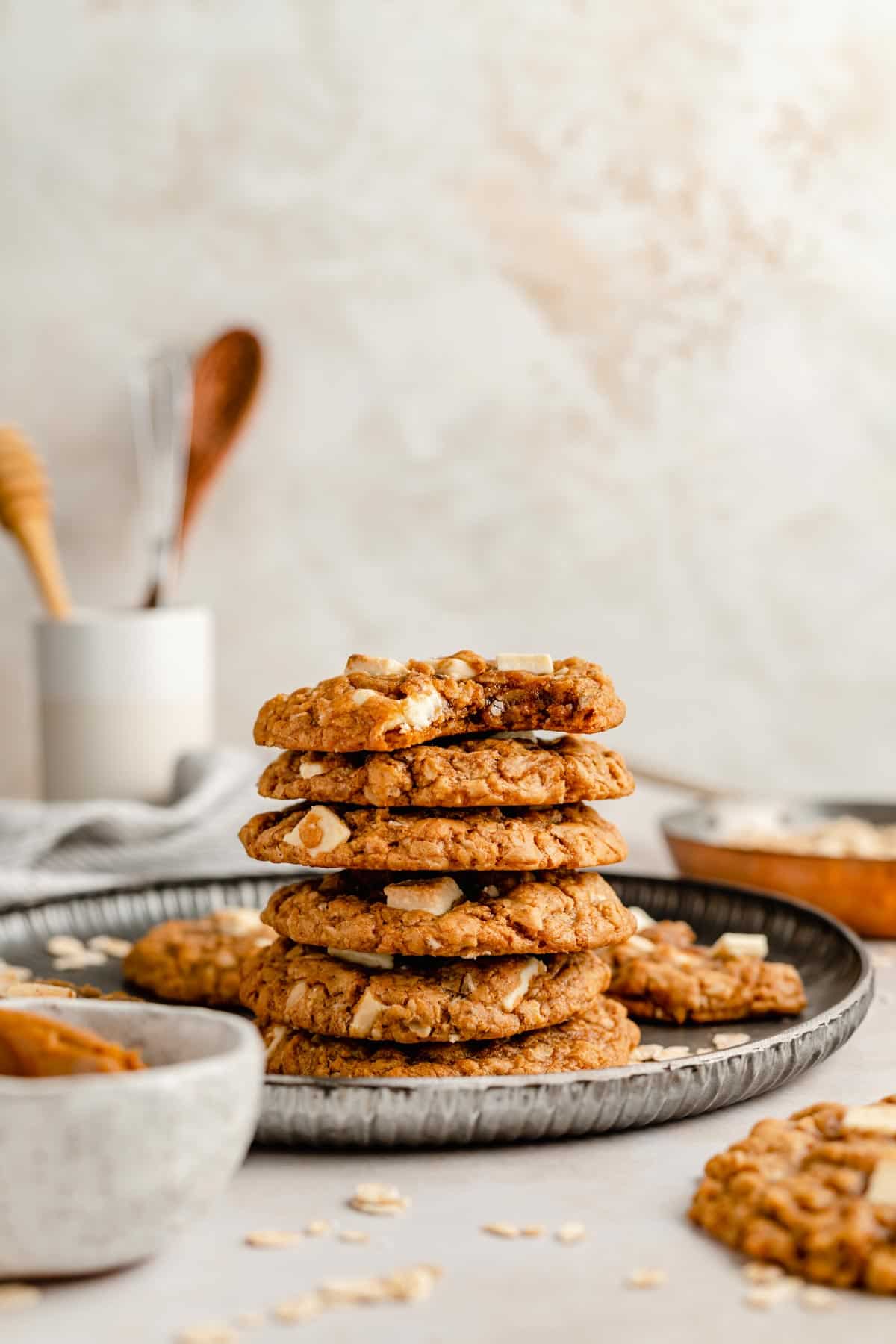 Stack of biscoff white chocolate chip oatmeal cookies on a plate with some utensils in a jar behind