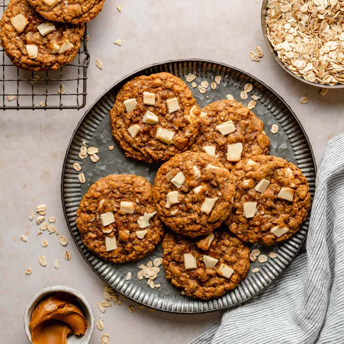 biscoff white chocolate chip oatmeal cookies on a plate with oats, napkin and a biscoff in a pot