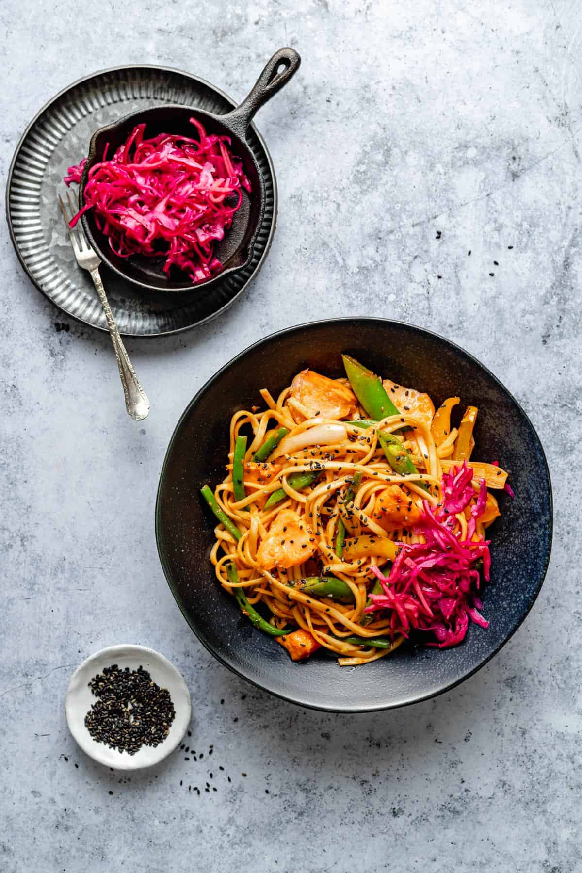 Gochujang Noodles in a bowl with salmon and a dish of quick pickle to the side.