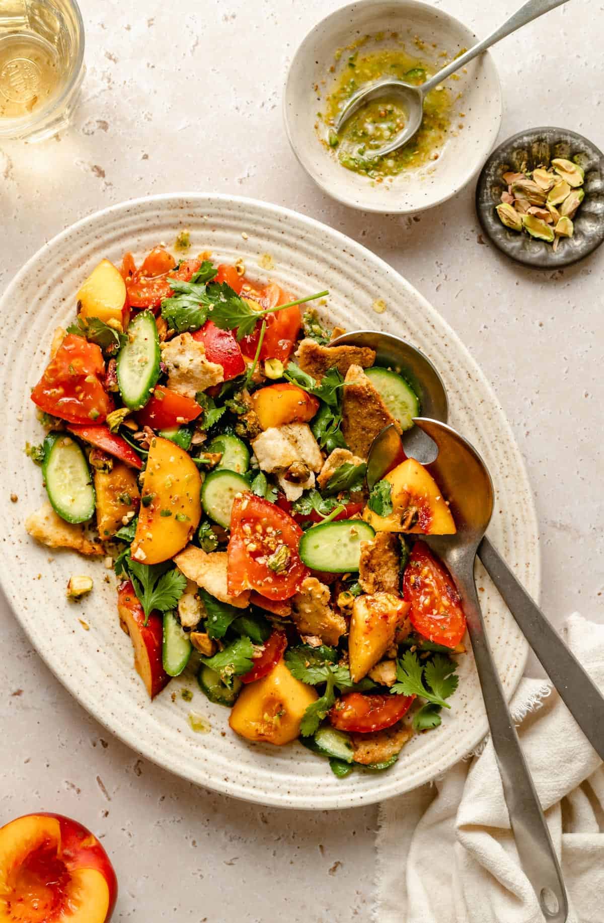 Dressed nectarine salad on a platter with two serving spoons and a napkin.