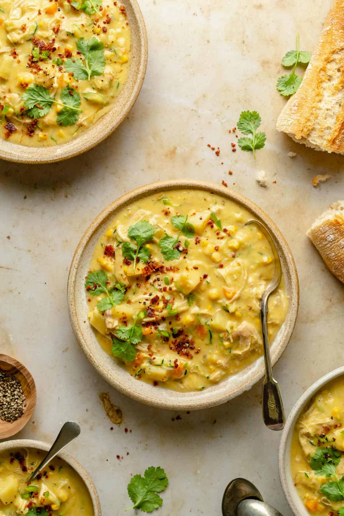 Chicken corn chowder served in various bowls with a spoon and bread on the side.