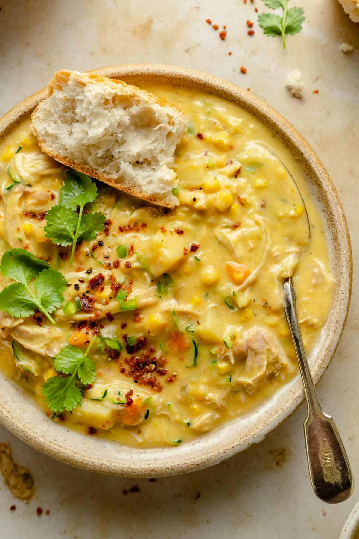 Close up of chicken corn soup in a bowl with a spoon, coriander and bacon crumbs on top.