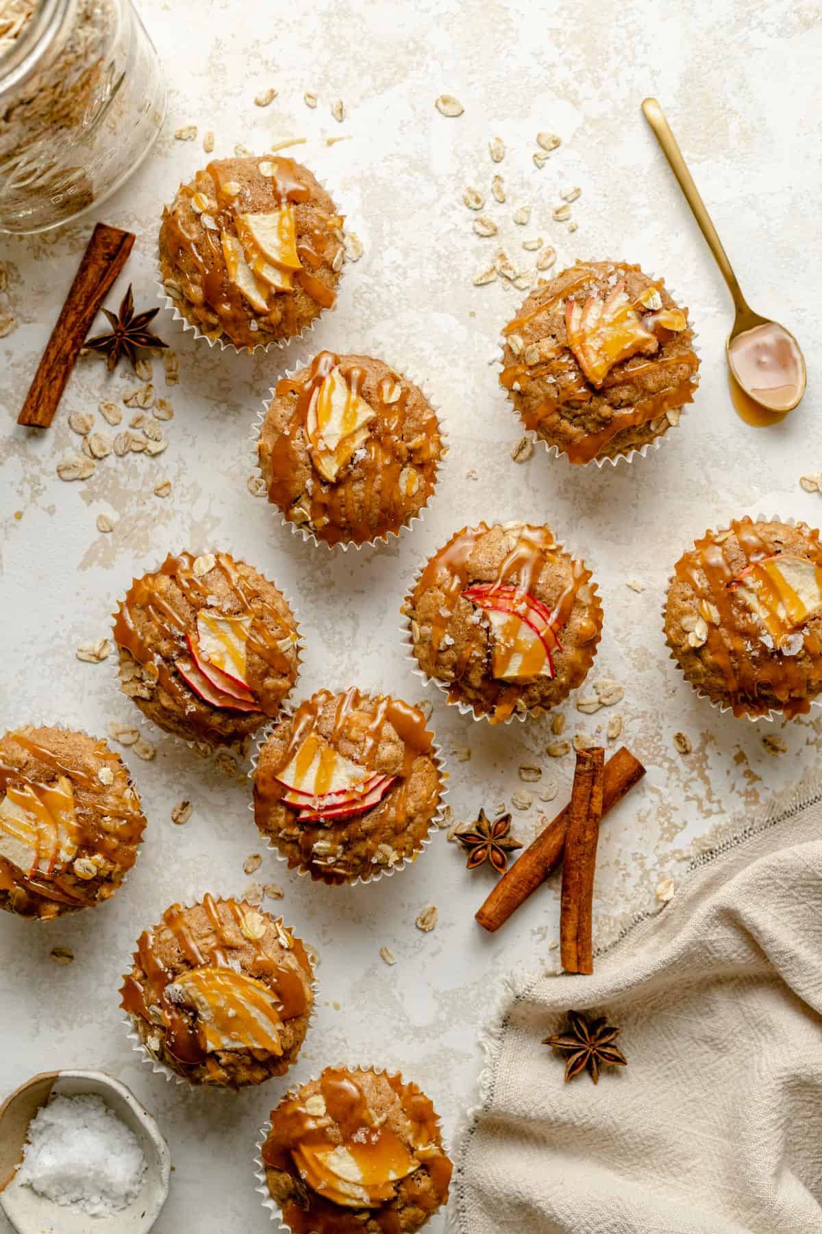 Array of apple oatmeal muffins with caramel drizzled on top and spices nearby.