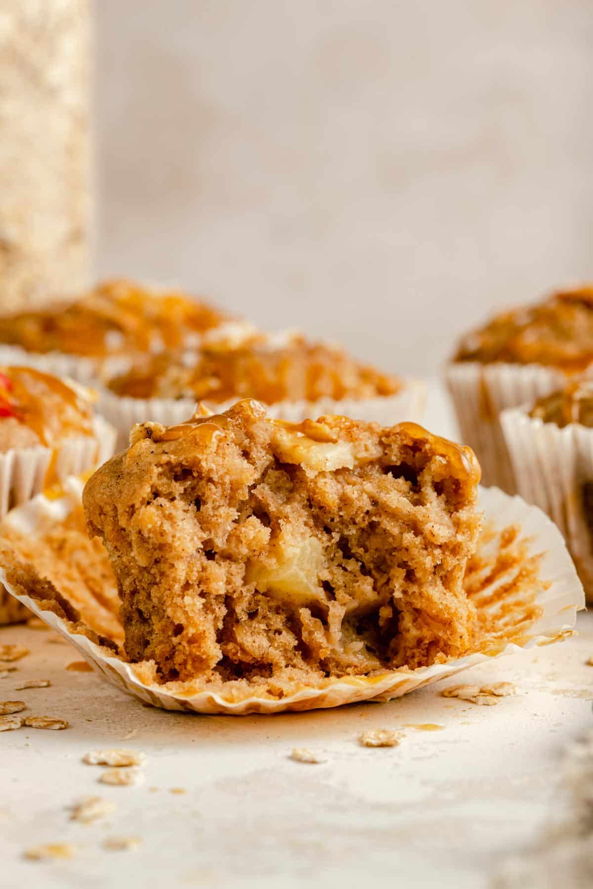 An apple oatmeal muffin with the casing peeled back and bite taken out of it showing the fluffy interior.