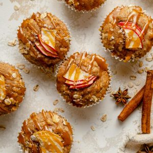 baked muffins with apple and caramel drizzled on top with cinnamon sticks nearby