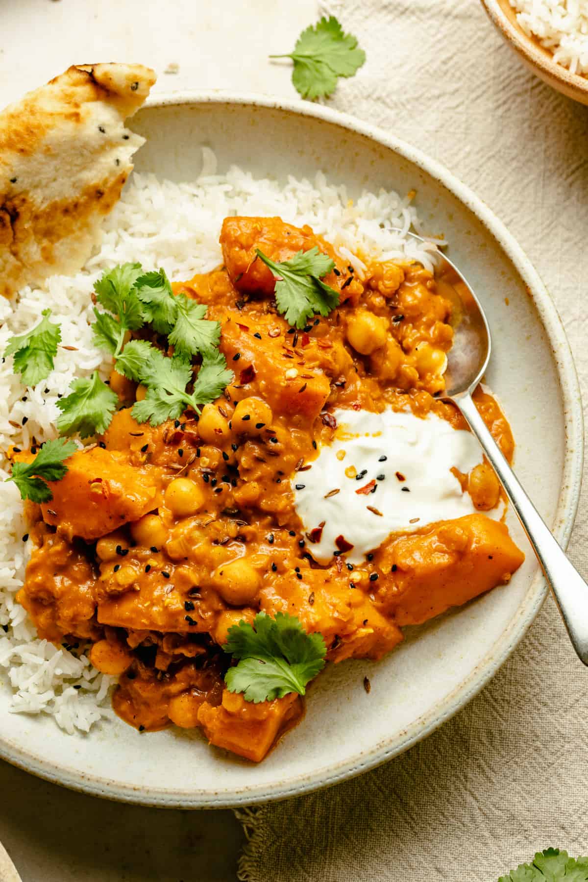 Butternut squash curry in a bowl served on basmati rice with yoghurt and naan.