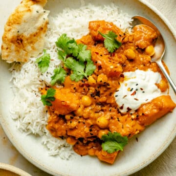 Butternut squash curry served in a bowl on rice with yoghurt, naan and a spoon.
