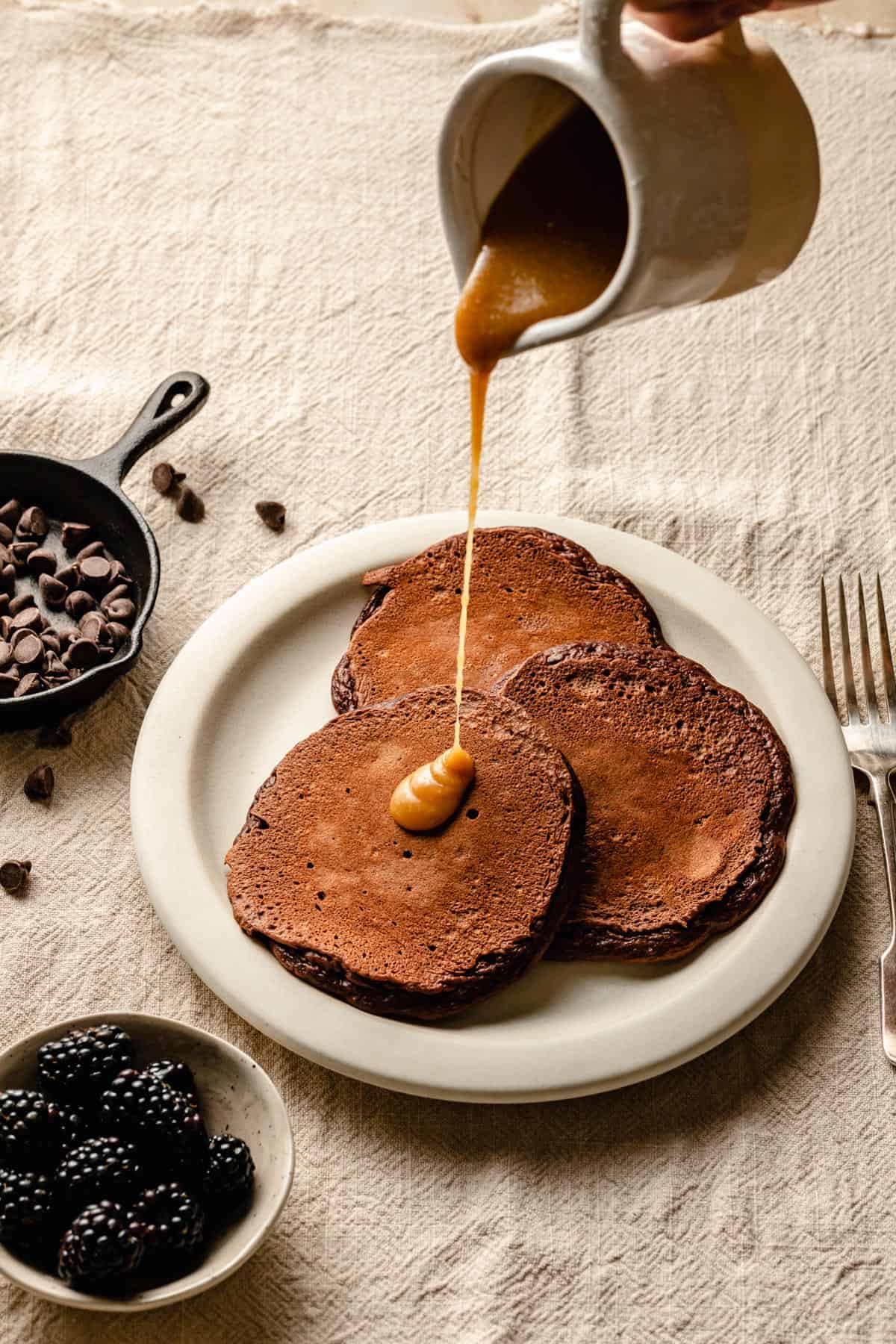 Pancakes made with cocoa powder on a plate with tahini maple syrup topping.