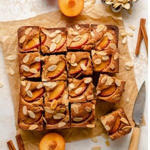 Plum and almond cake sliced up into portions with spices, plums and almonds around