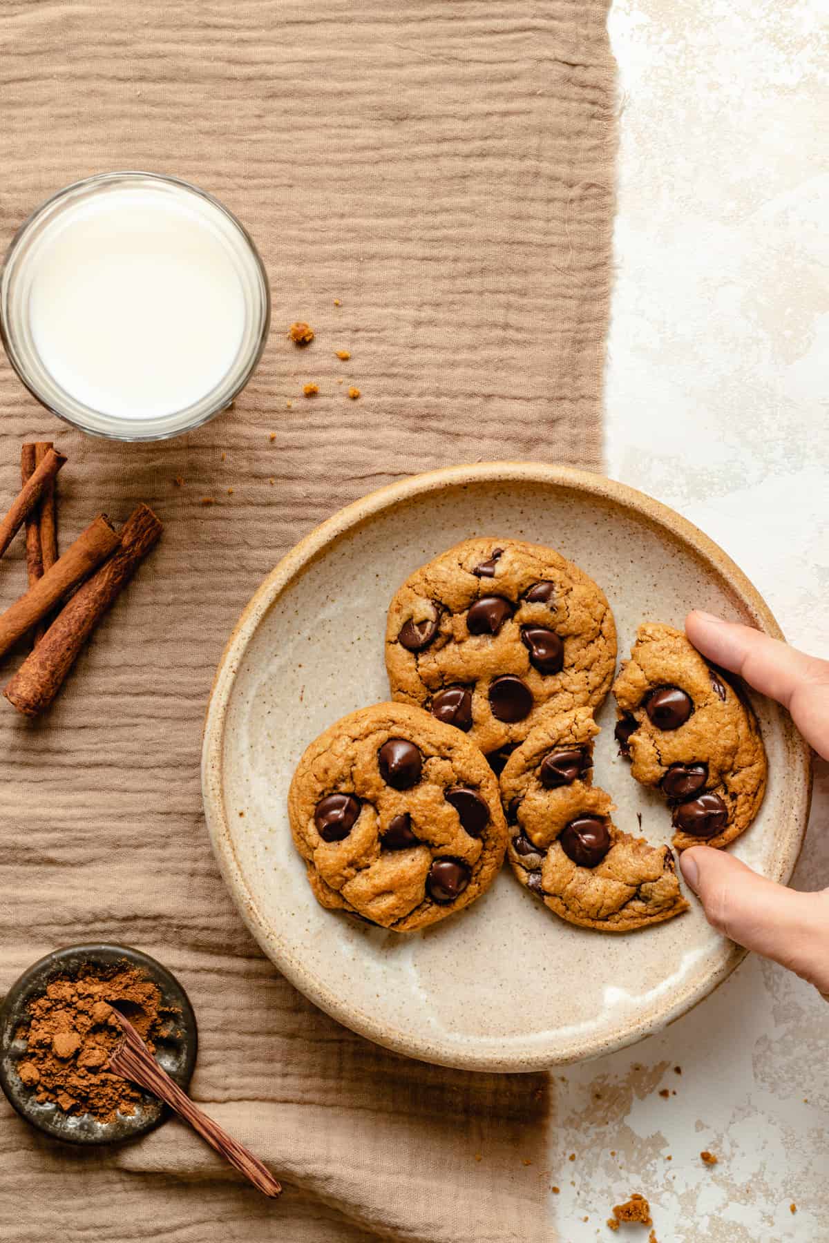 A plate of easy chewy cookies with one broken and being picked up, with pumpkin spice surrounding it.