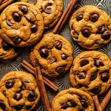 A tray of pumpkin chocolate chip cookies with cinnamon sticks scattered amongst them.