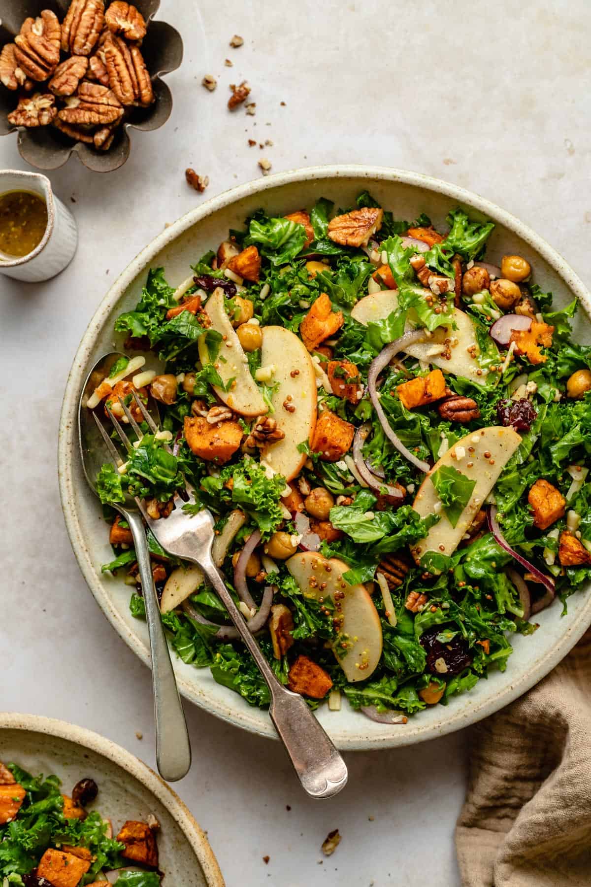 Warm sweet potato kale salad in a serving bowl with a spoon and fork and a jug of dressing.