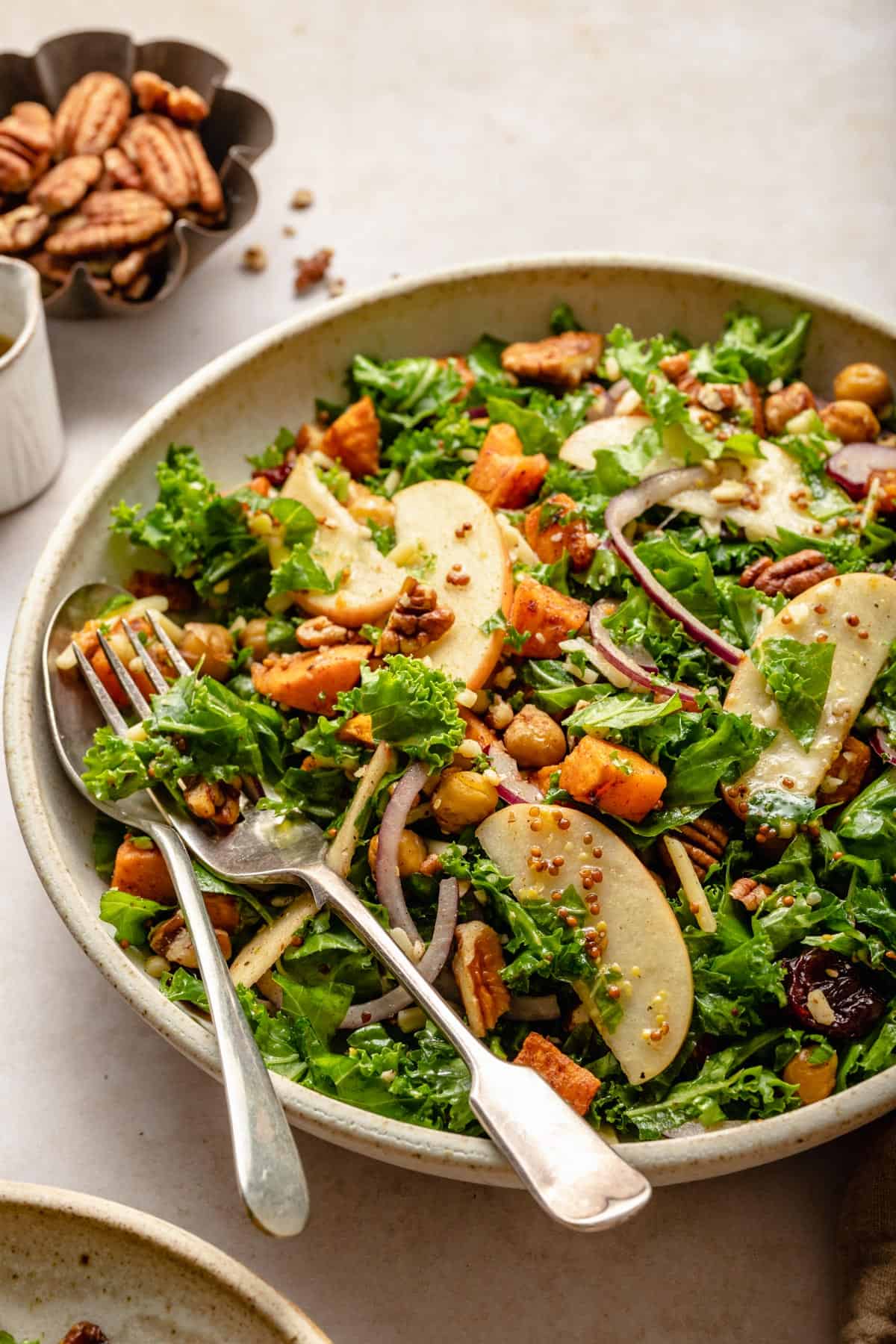 Kale salad with apples, chickpeas and   red onion with a spoon and fork in a bowl.