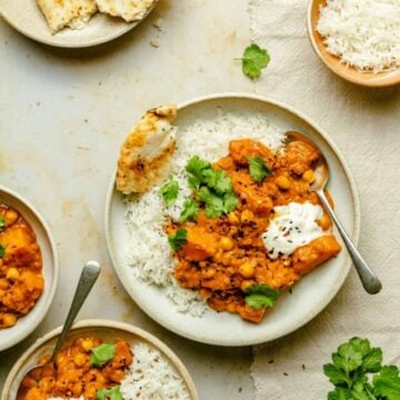 Multiple bowls of butternut squash curry with rice, naan and spoons.