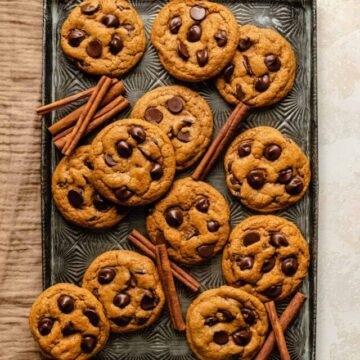 Pumpkin Chocolate Chip Cookies on a sheet pan with cinnamon sticks and a napkin.