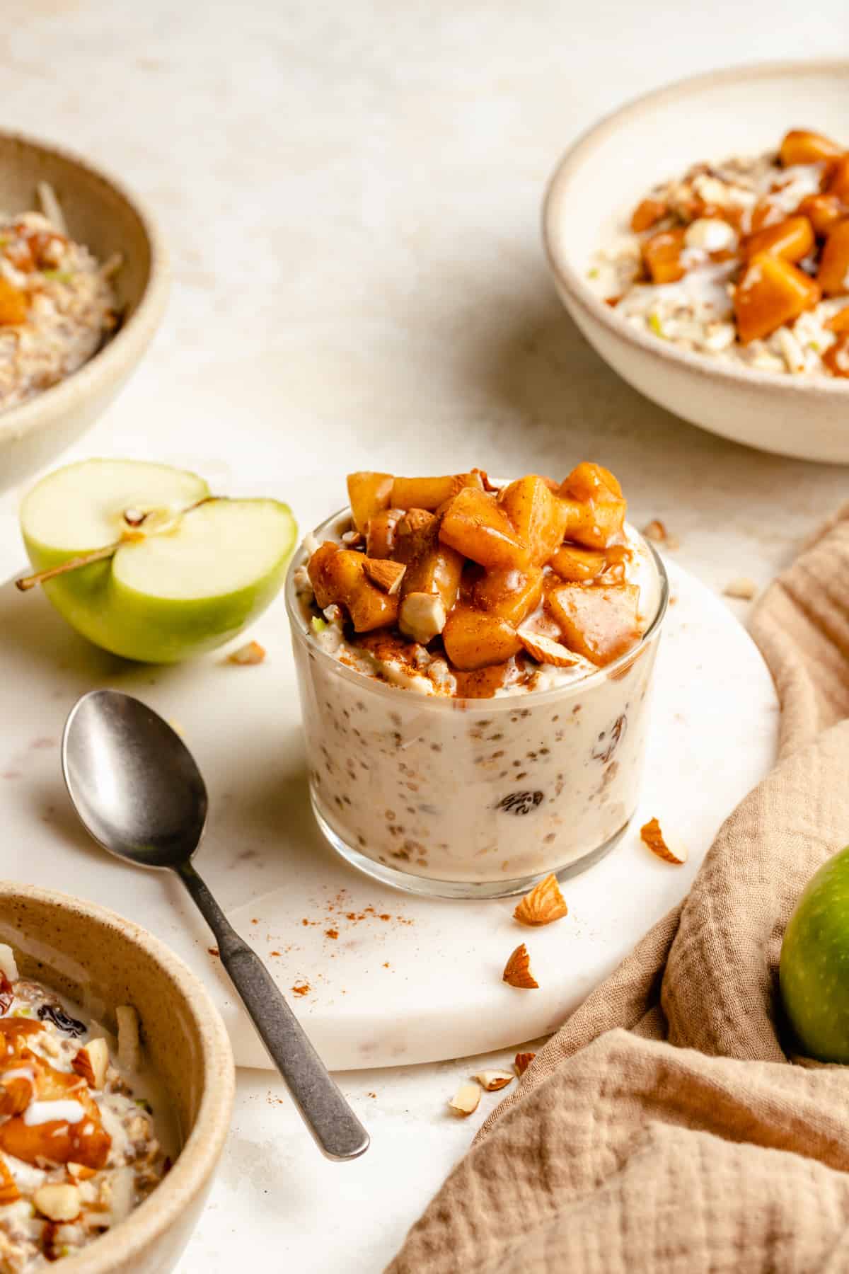 A jar of overnight oats on a marble board with an apple and spoon to the side. 