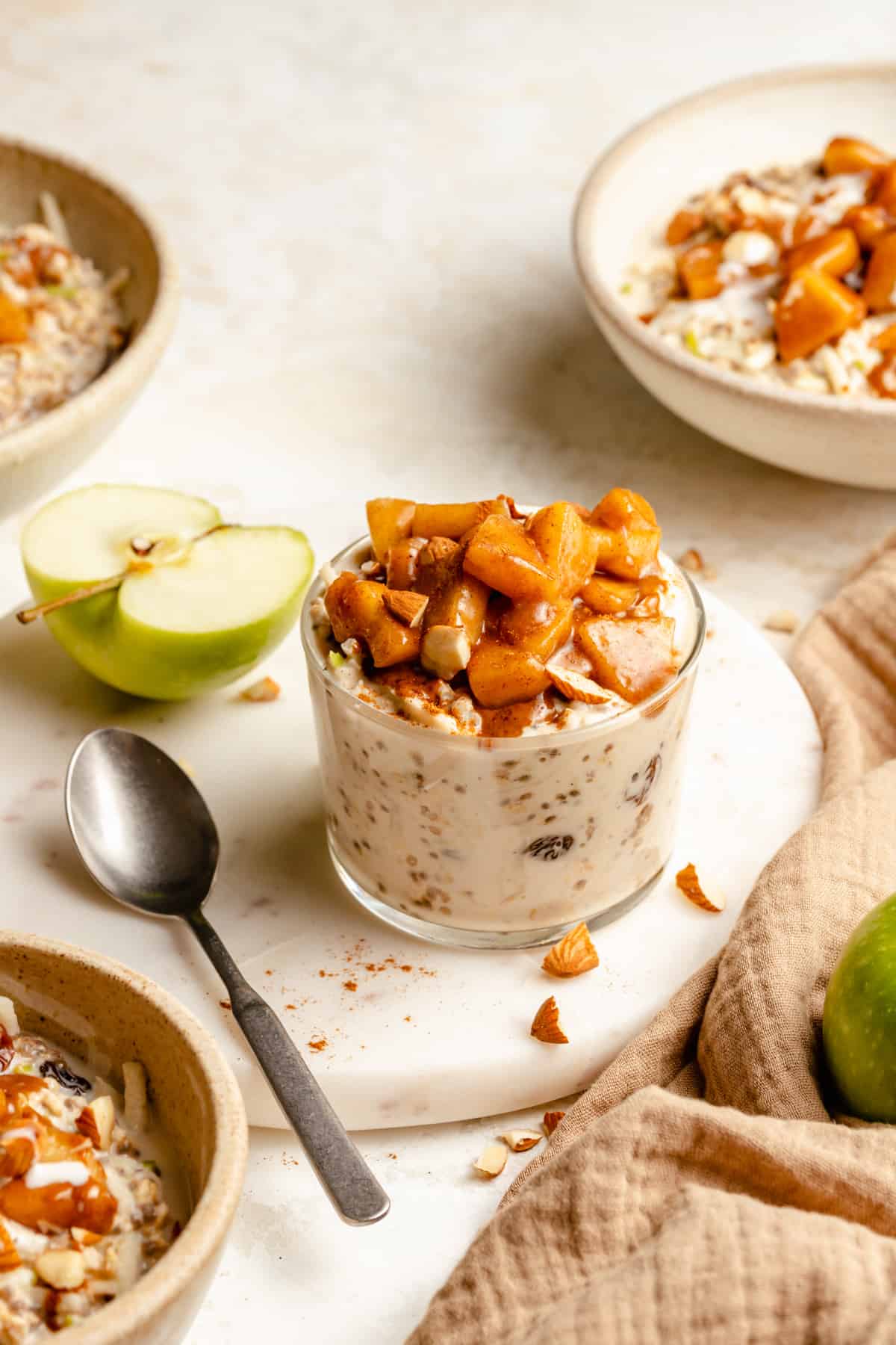 A jar of overnight oats on a marble board with an apple and spoon to the side.