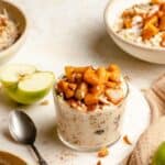 A jar of overnight oats on a marble board with a spoon and apple to the side.