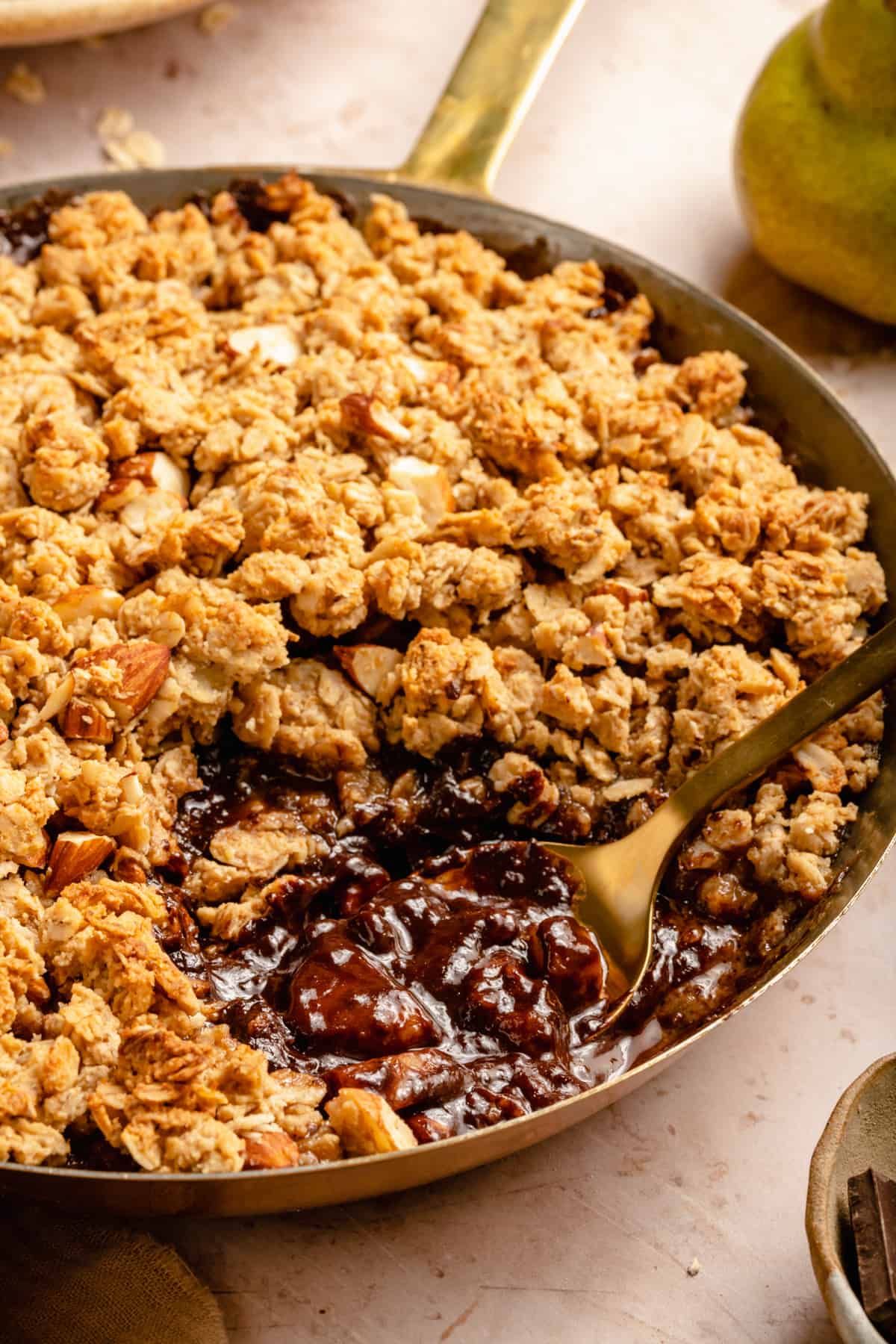 A spoon taking out a serving of crumble oozing with pears and chocolate with an oat and almond crumble topping.