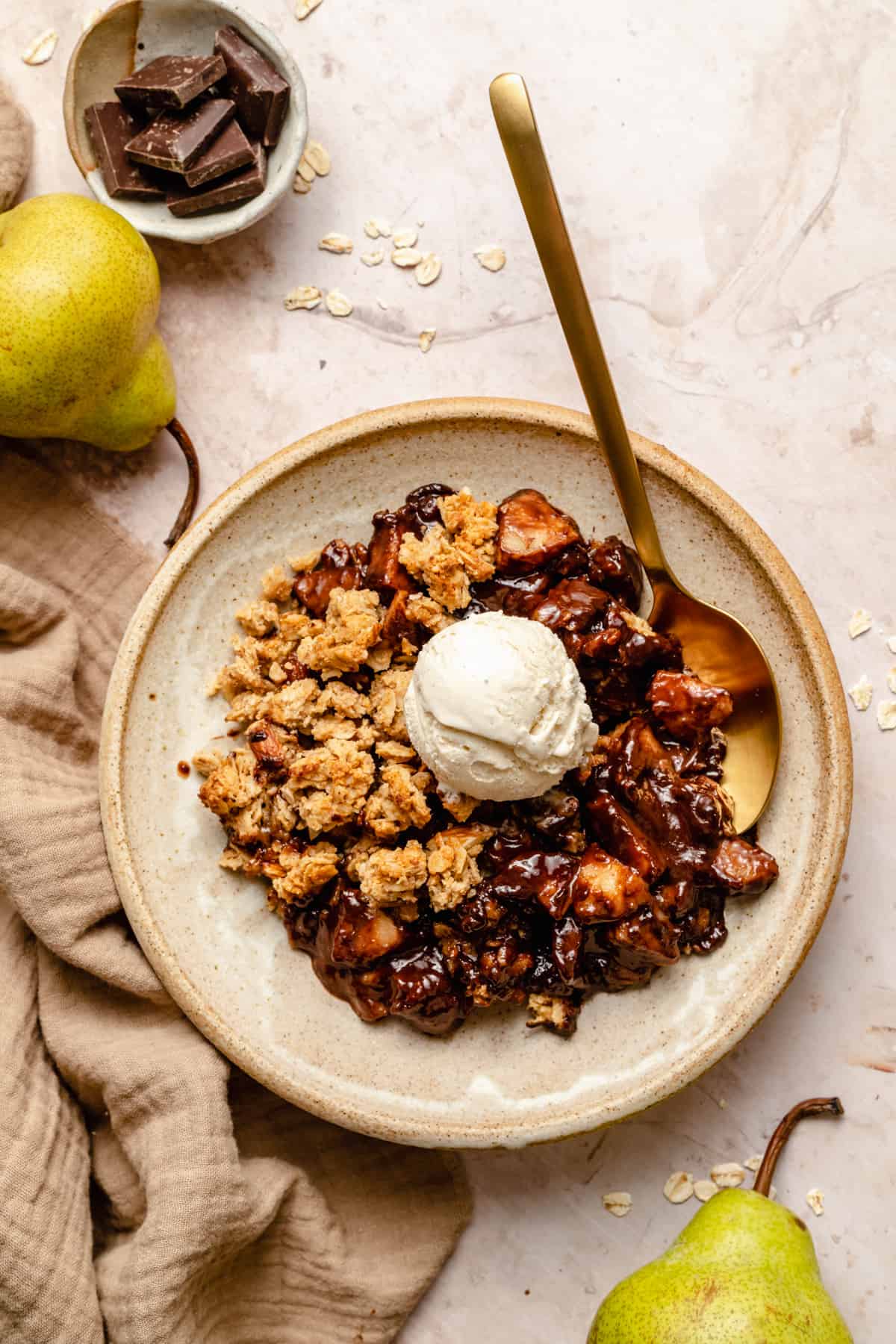 Pear crumble served up with chocolate sauce and ice cream on top with spoon and pears on the side.