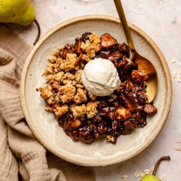 Pear and chocolate crumble served in a bowl with a spoon and a scoop of ice cream on top.