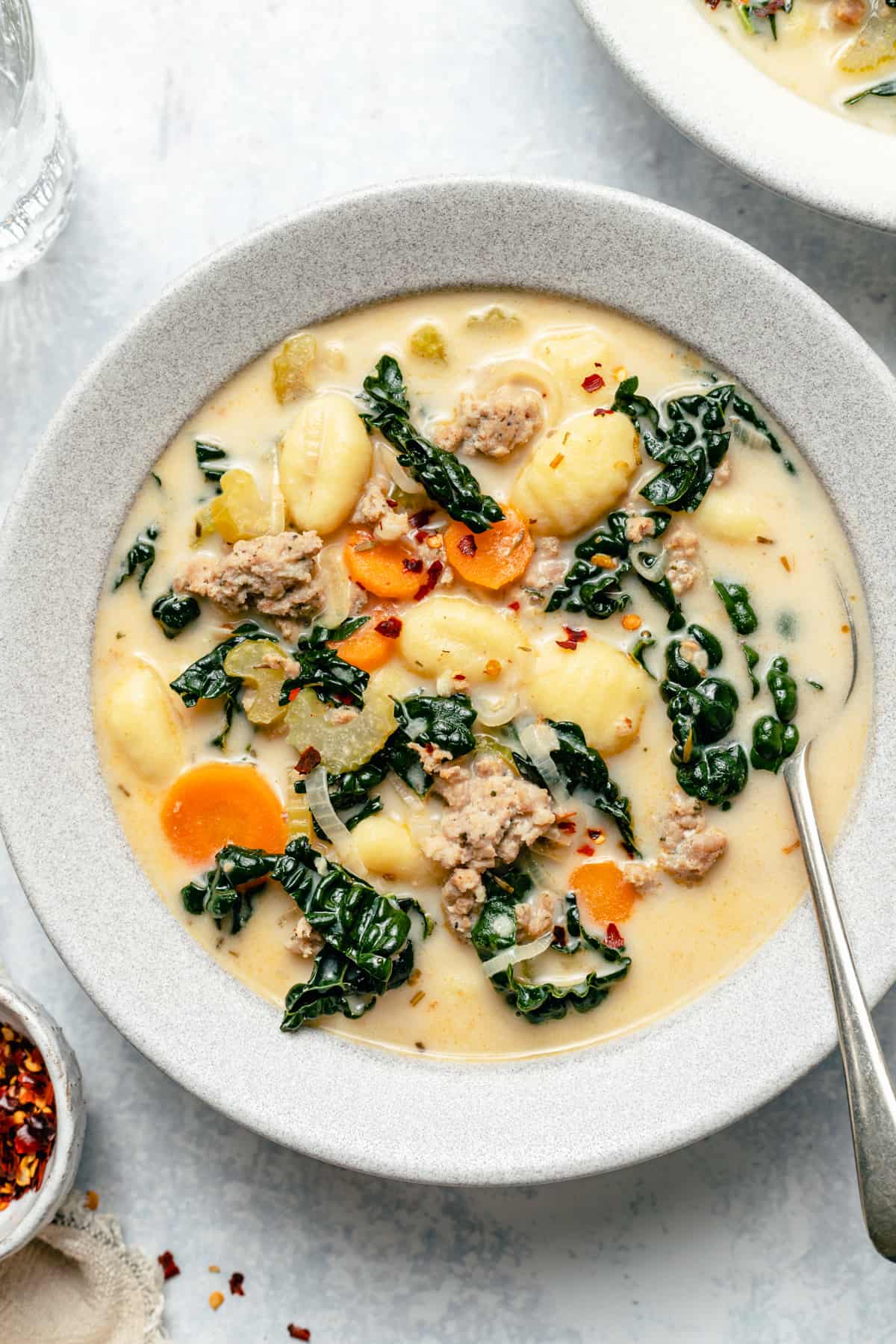 A bowl of sausage gnocchi soup with a spoon and a napkin.