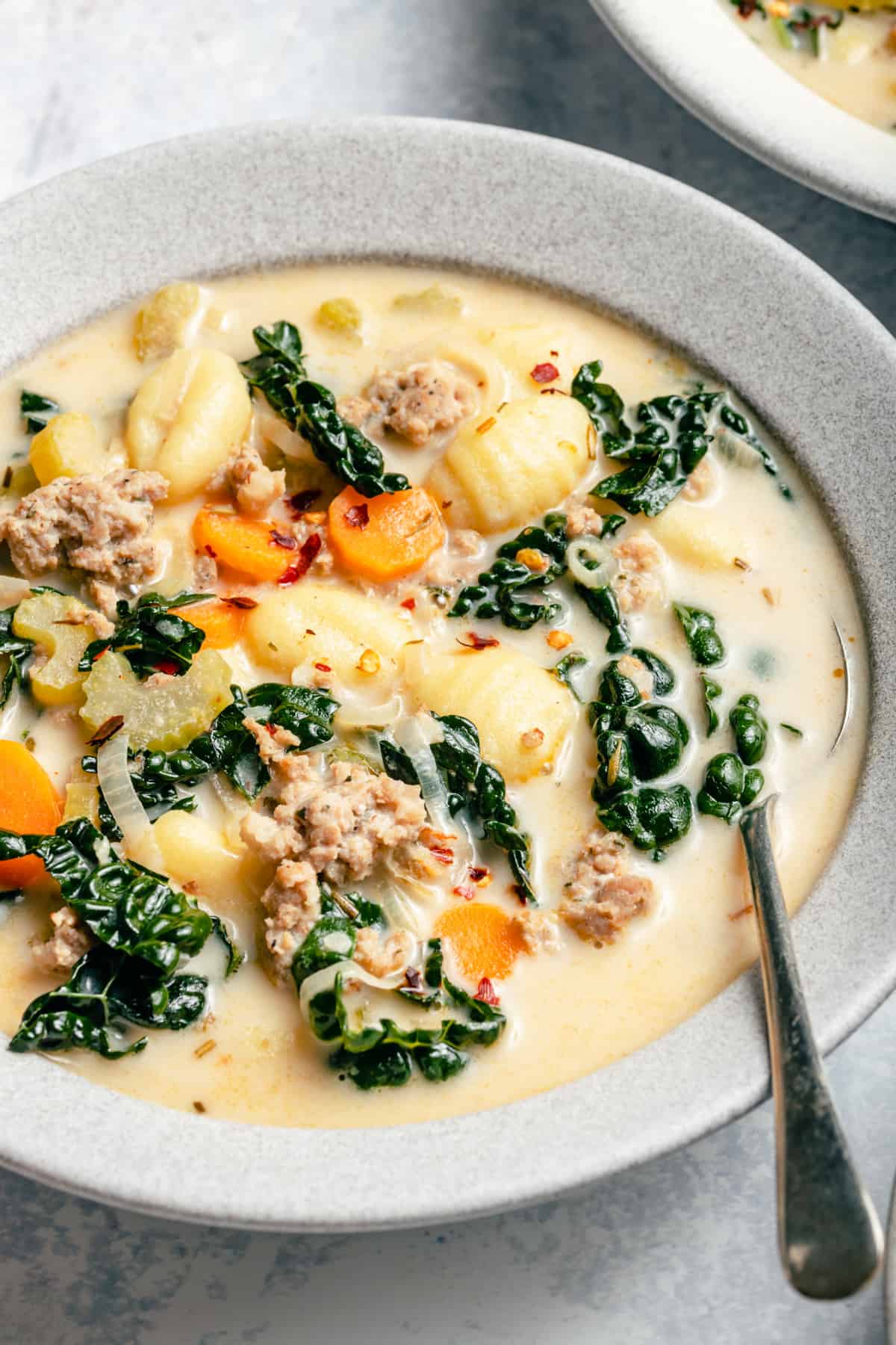 A bowl of creamy gnocchi soup with sausage, kale, gnocchi, celery and carrots on top with a spoon.