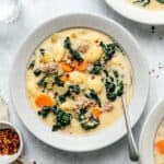 Sausage Gnocchi Soup in a bowl with a spoon and a bowl of chilli flakes to the side.