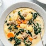 Close up of a bowl of sausage gnocchi soup with a spoon in the bowl.