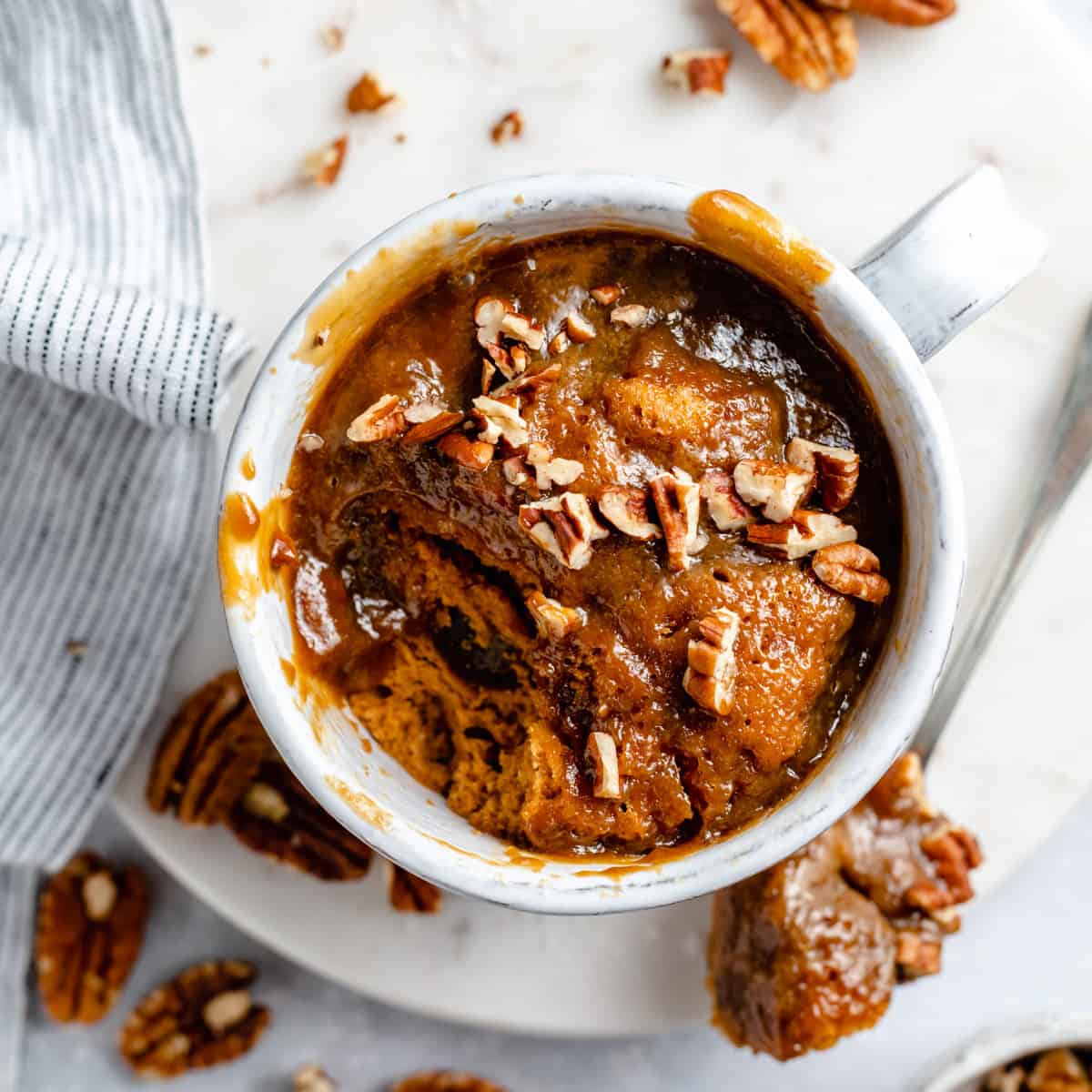 Sticky toffee pudding mug cake on a marble board with a spoon taken out of showing the sauce.