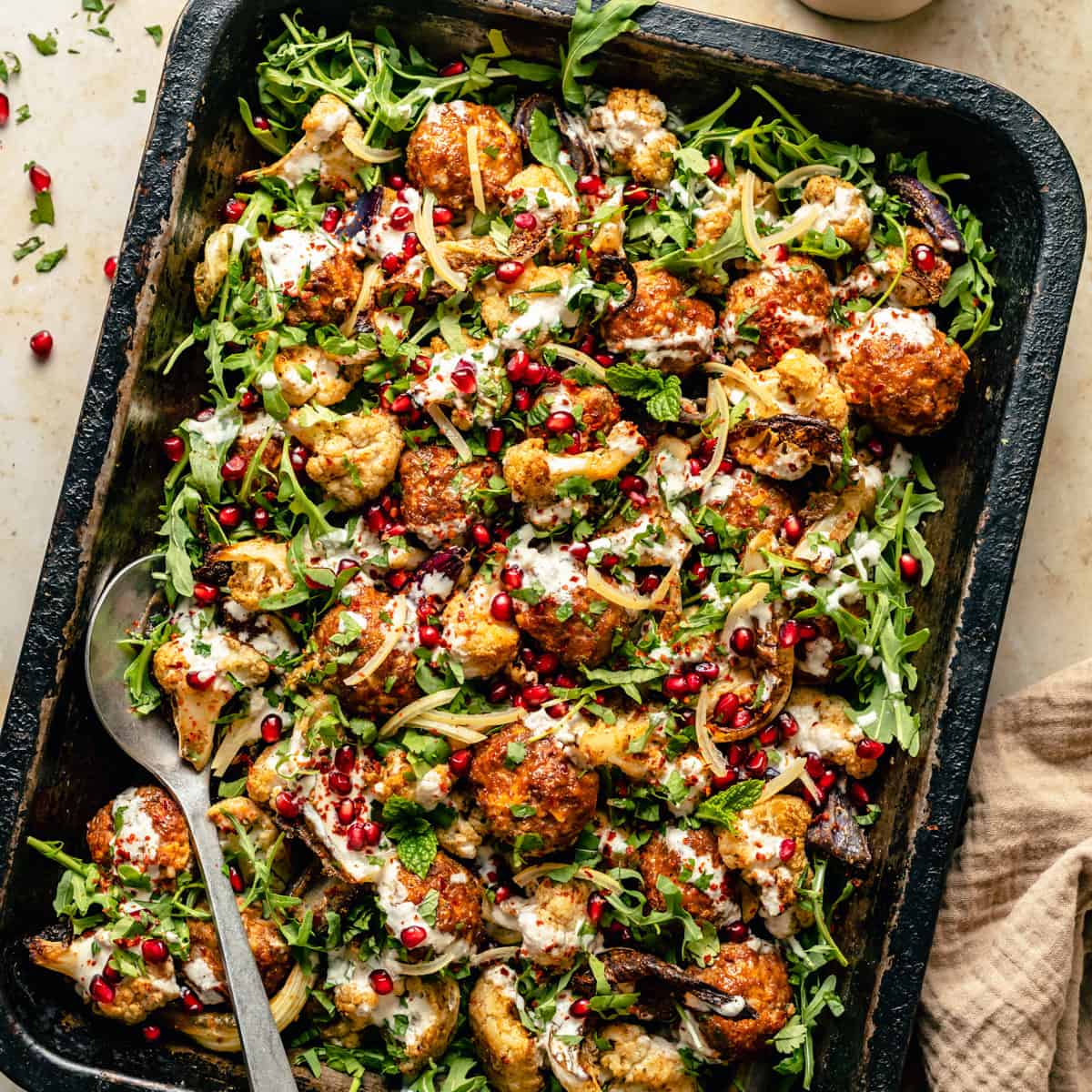A sheet pan with baked turkey meatballs and roasted cauliflower with yoghurt dressing on top.