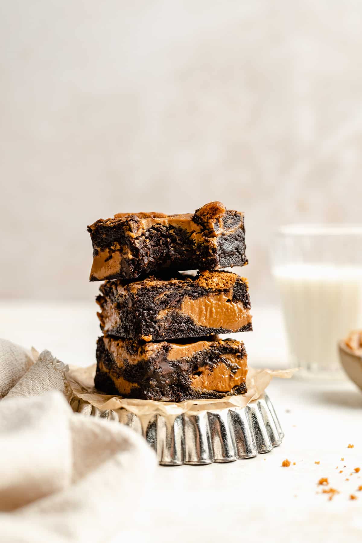 A stack of gooey fudgy biscoff brownies on a metal dish with one on top with a bite taken out showing the insides.