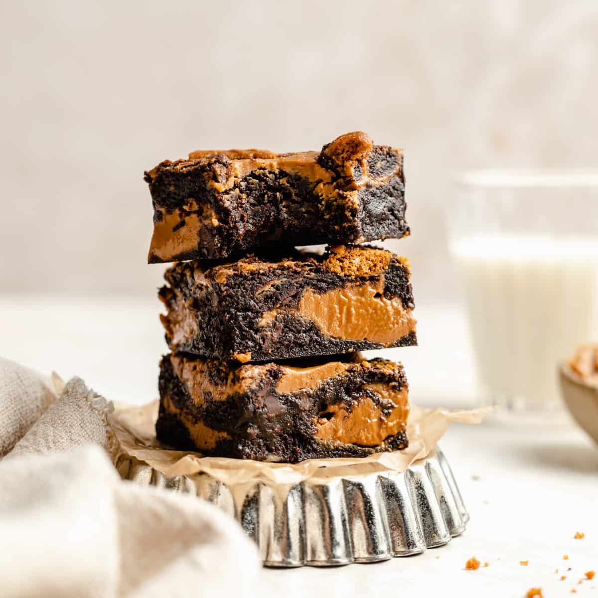 A stack of gooey fudgy biscoff brownies on a metal dish with the one of top with a bite taken out.