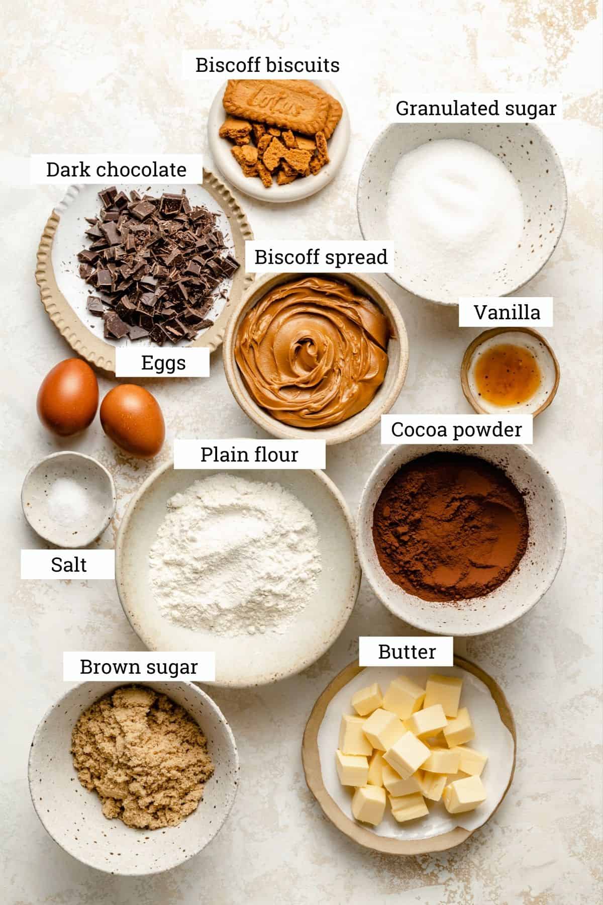 An array of bowls of ingredients to make biscoff brownies including, cocoa powder, sugar, flour, butter. 