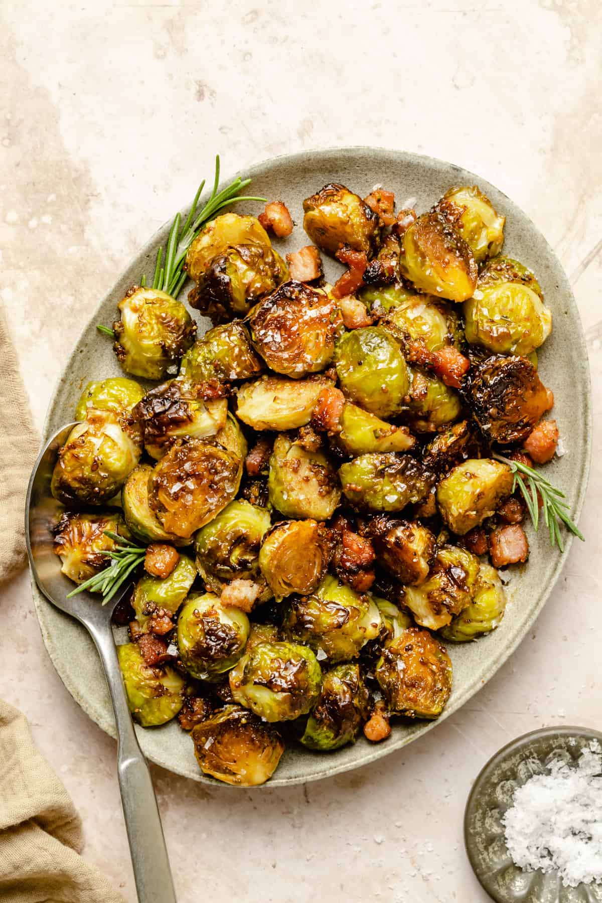 A plate of caramelized brussels sprouts with bacon and maple syrup with rosemary sprigs and a spoon. 