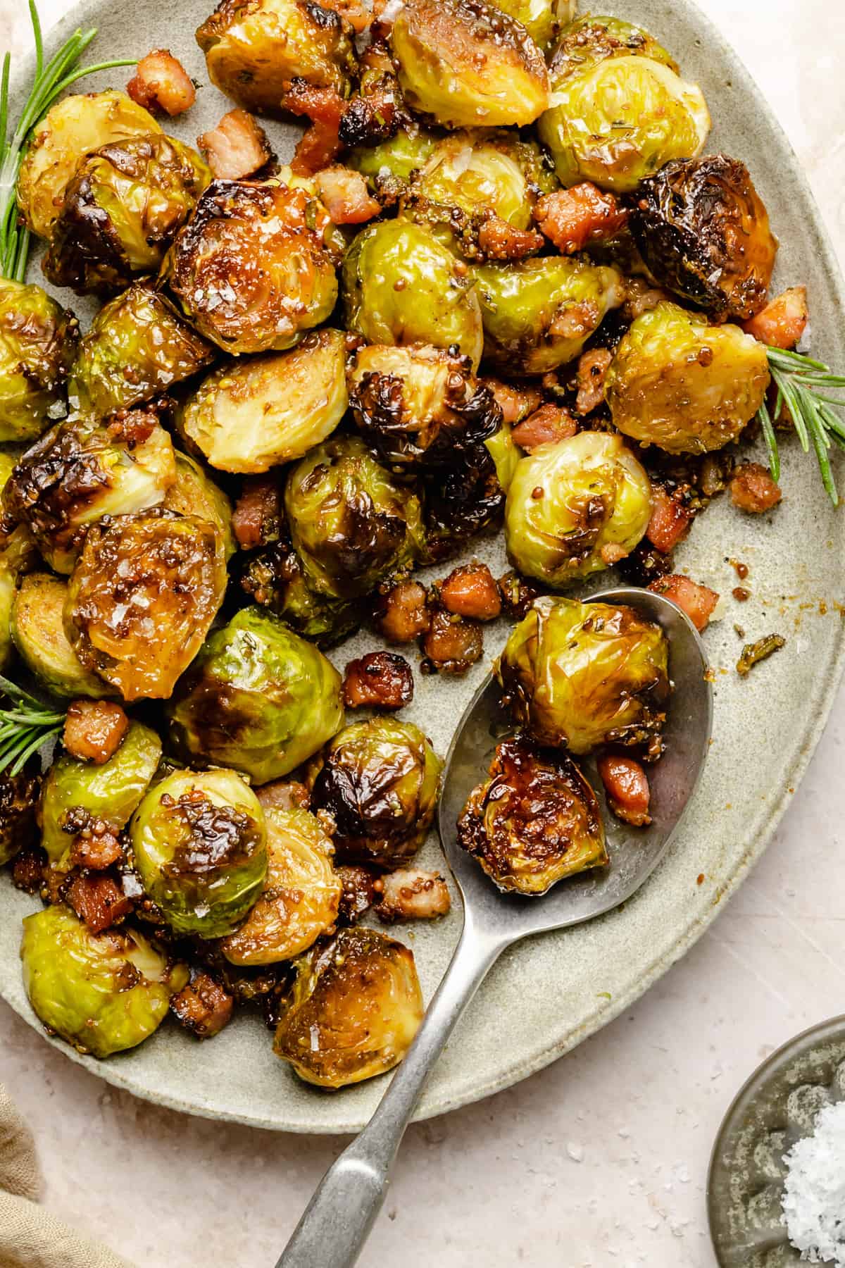 A serving plate of caramelized brussels sprouts with bacon and rosemary with a spoon serving them up. 