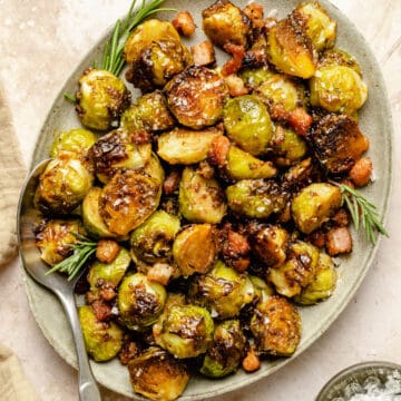 Caramelized brussels sprouts with bacon and maple syrup on a plate with a spoon and rosemary sprigs.