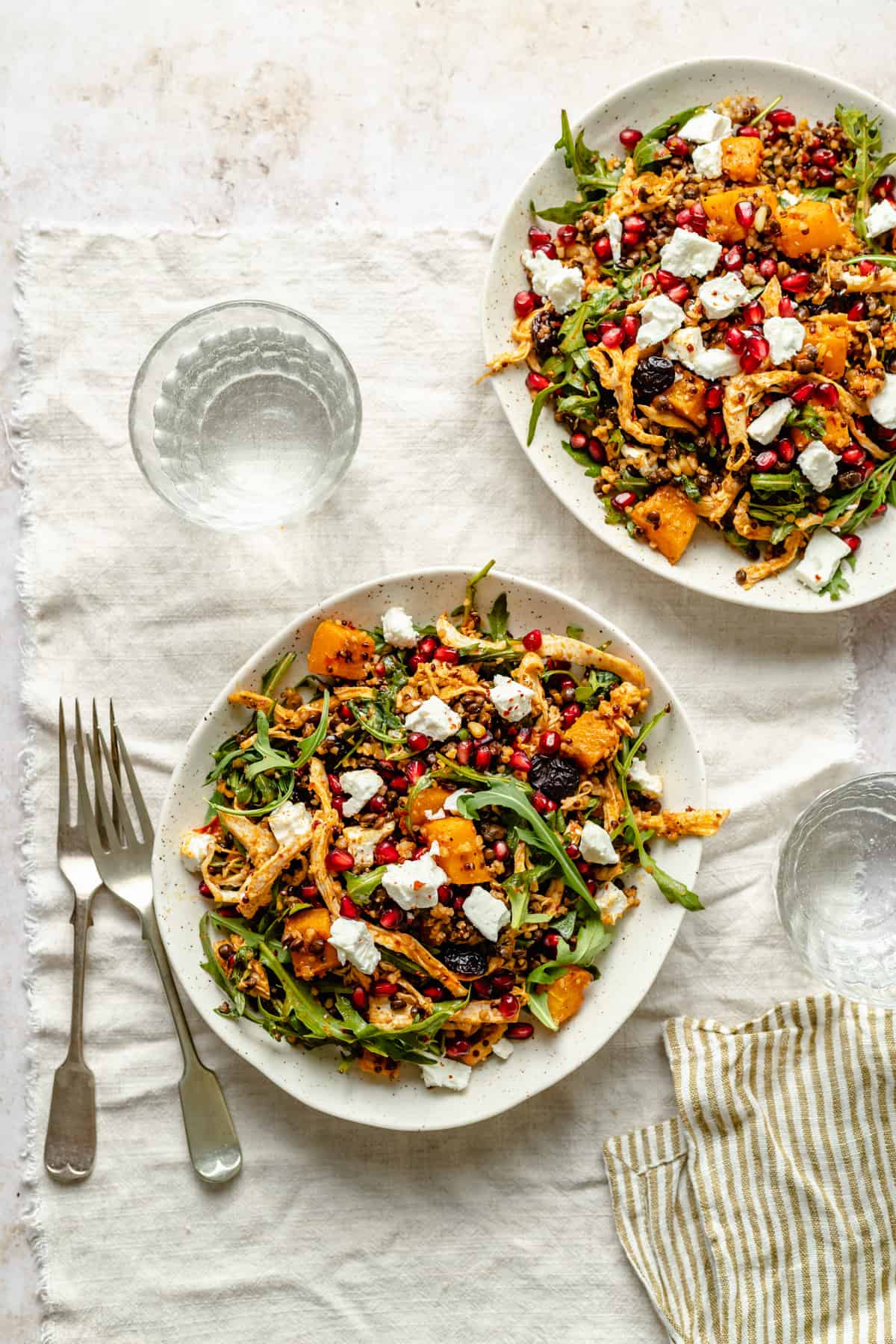 Fall grain salad served on two plates, with forks and glasses of water nearby.