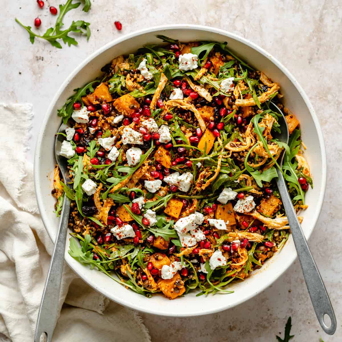 A large serving bowl with serving spoons about to toss the fall grain salad together. 