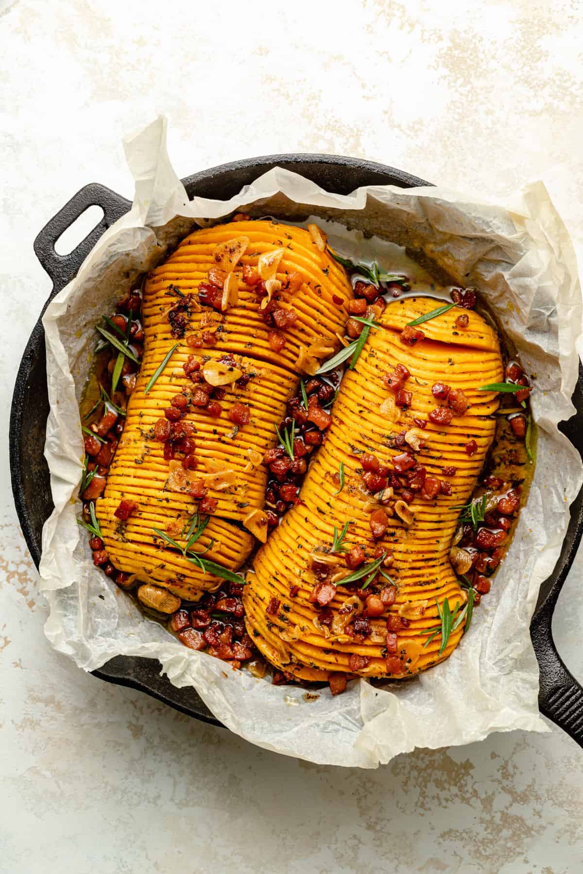roasted hasselback squash served in the skillet with bacon brown butter poured over the top.