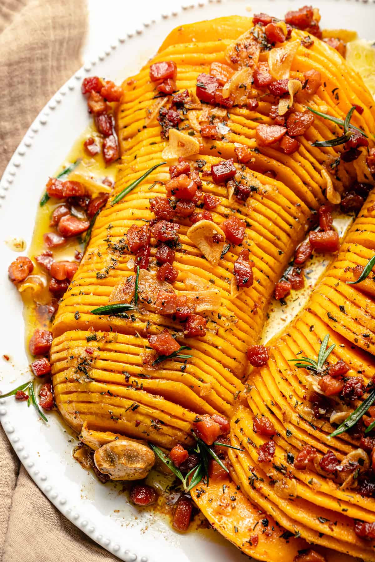Close up showing crispy pancetta and garlic on top of the hasselback squash on a platter.