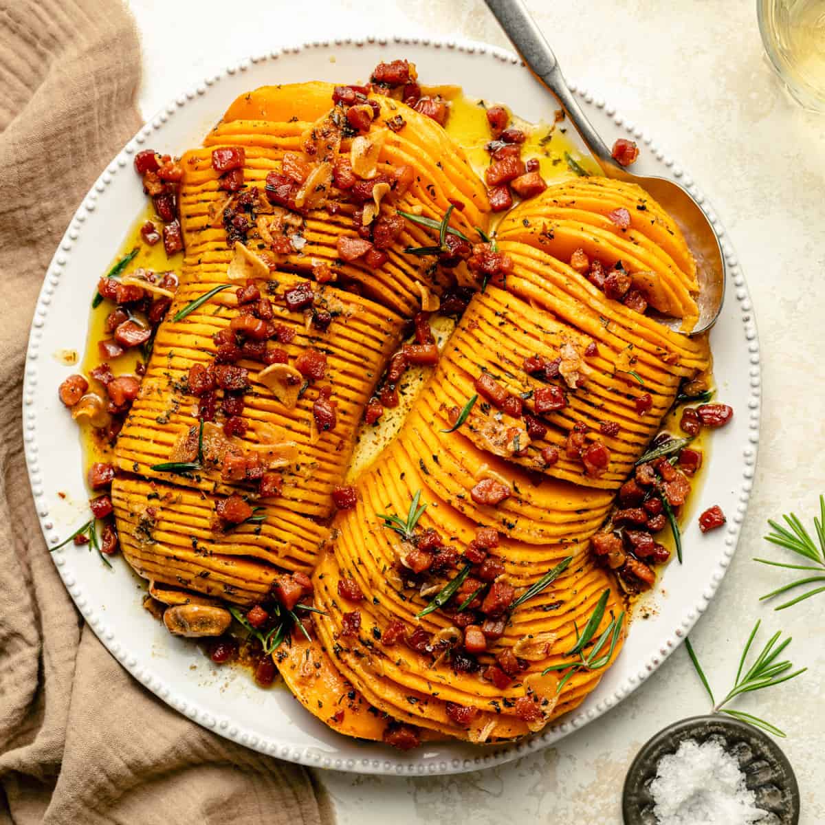 Hasselback Butternut Squash on a platter with bacon brown butter poured over the top and a spoon. 