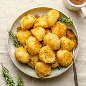 The BEST Crispy Rosemary Roasted Potatoes in a bowl with a serving spoon and a jug of gravy to the side.